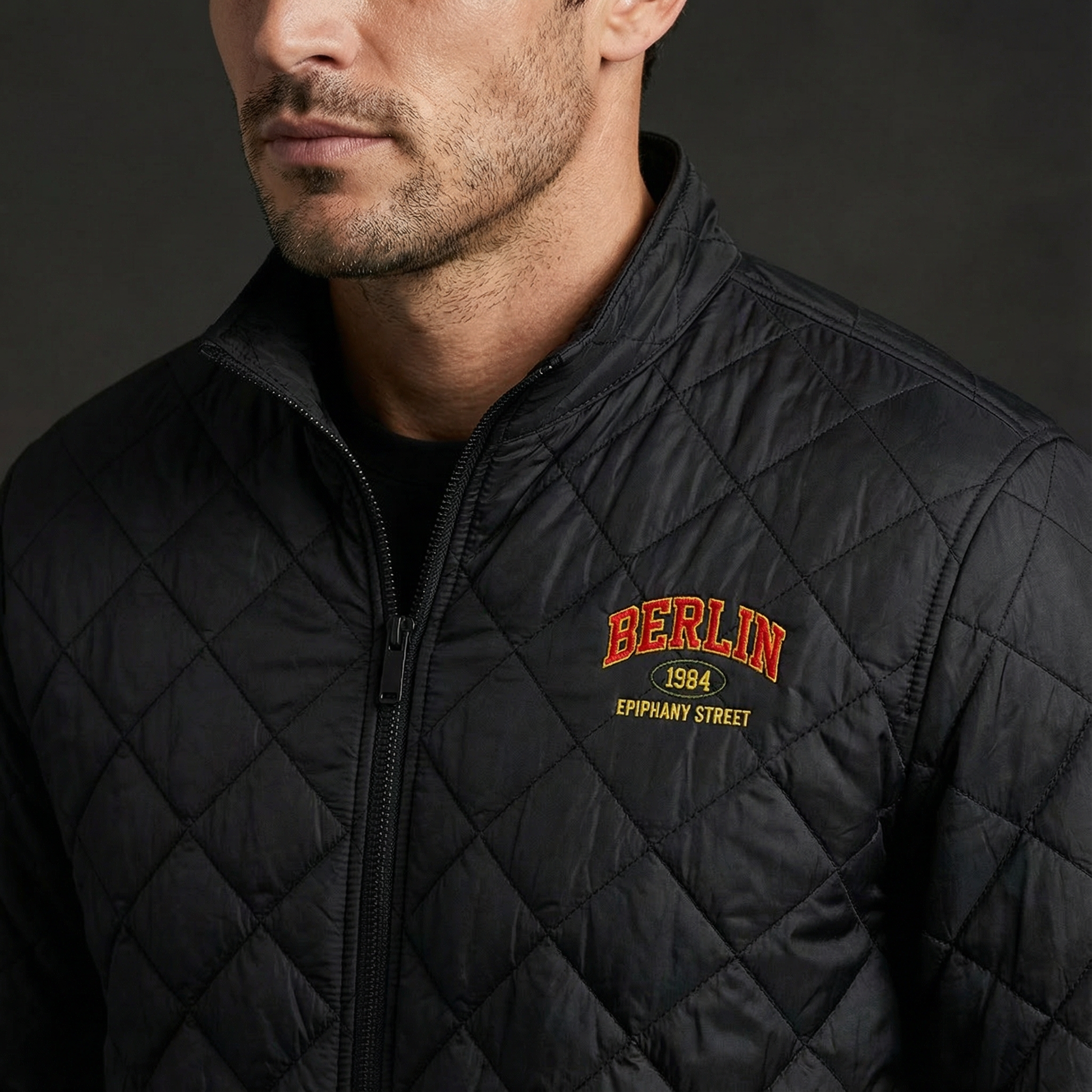 Man wearing a black quilted jacket with 'Berlin 1984' text on a dark background