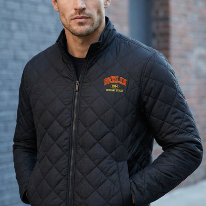 Man wearing a black quilted jacket with 'Berlin' branding against a brick wall.