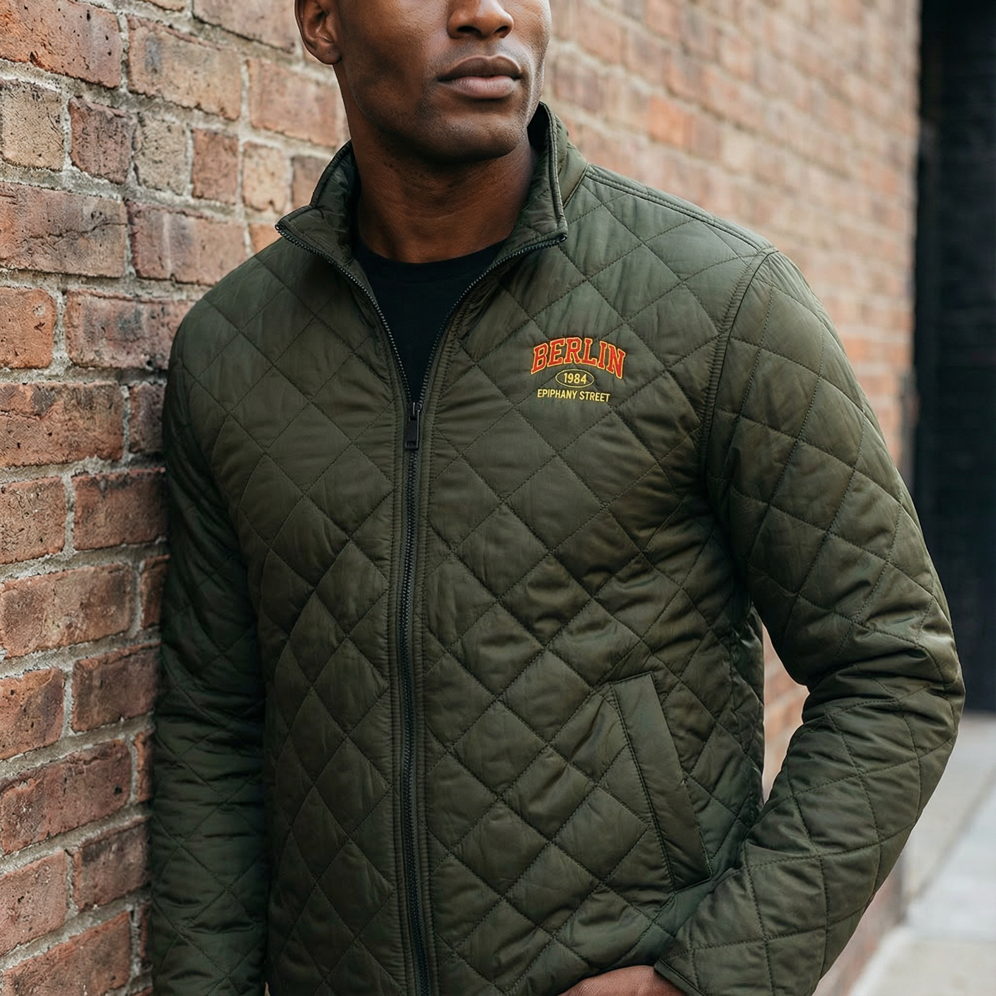 Man wearing a green quilted jacket with 'Berlin' branding against a brick wall.