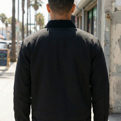 Person wearing a black jacket walking on a street with palm trees in the background
